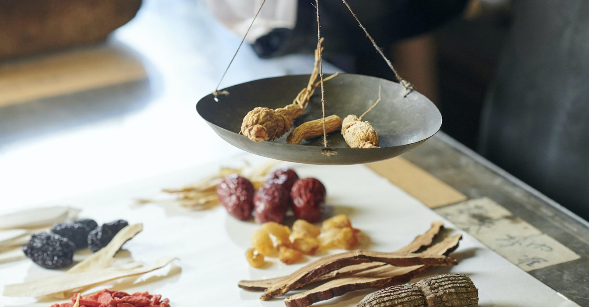 Hands of tradiotional Asian medicine practitioner weighting herbs and roots on ol scales